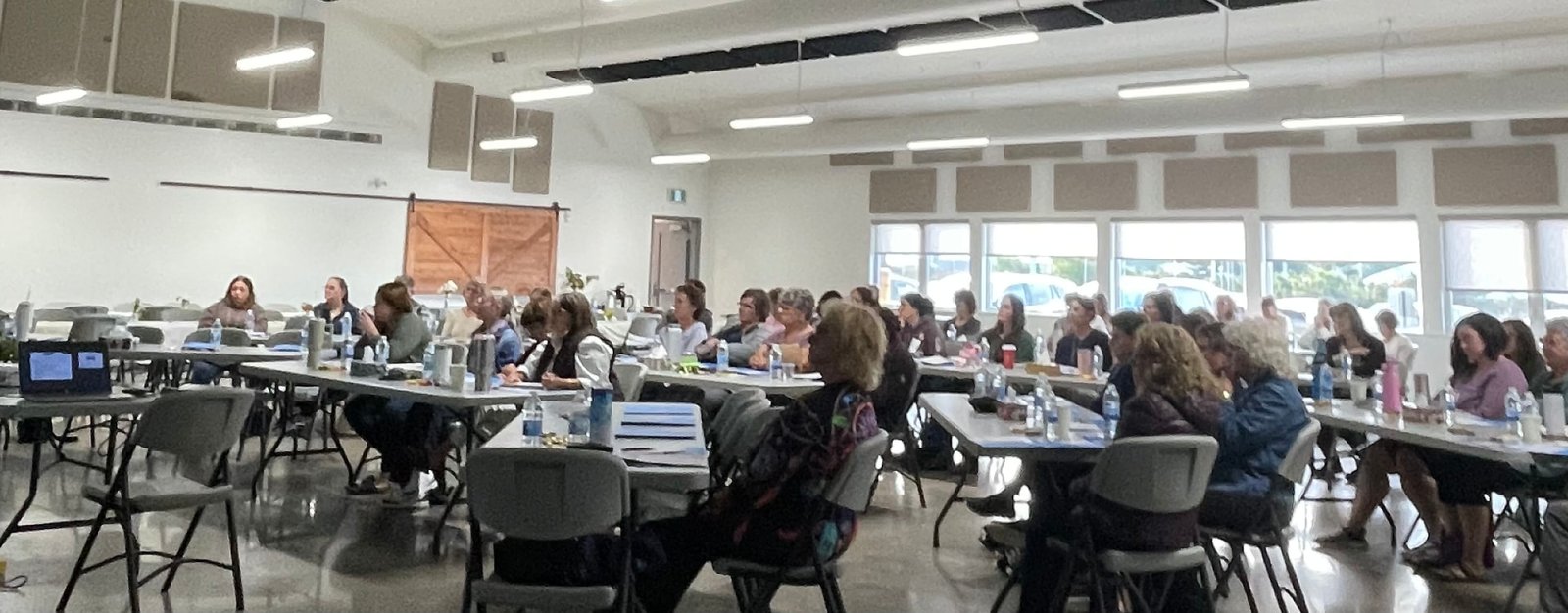 Attendees seated at long tables in the community room for the first “Let’s Talk About Grief, Loss & Palliative Care” Grief Literacy Education Day.
